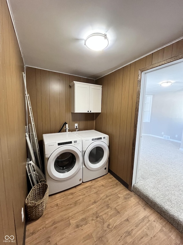 washroom featuring separate washer and dryer, light hardwood / wood-style floors, cabinets, and wood walls