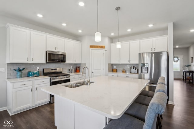 kitchen with appliances with stainless steel finishes, decorative light fixtures, sink, white cabinets, and a kitchen island with sink