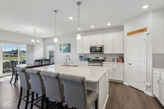 kitchen featuring decorative light fixtures, an island with sink, sink, white cabinets, and stainless steel appliances