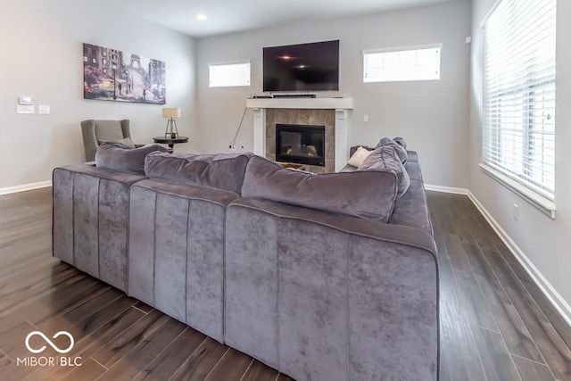 living room featuring a tiled fireplace, a healthy amount of sunlight, and dark hardwood / wood-style flooring