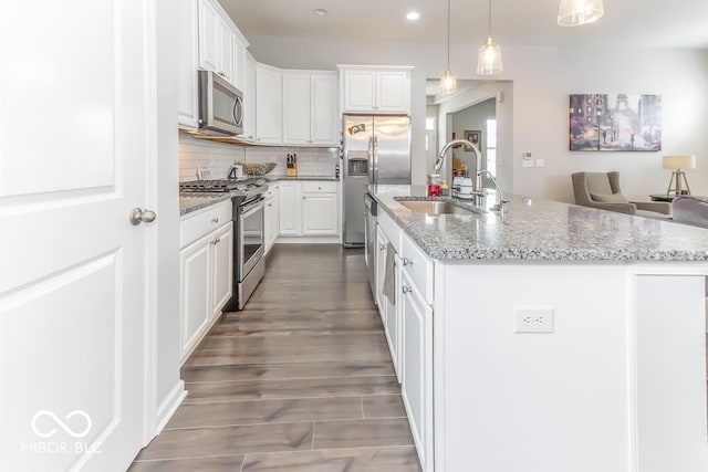 kitchen with white cabinetry, hanging light fixtures, an island with sink, stainless steel appliances, and light stone countertops