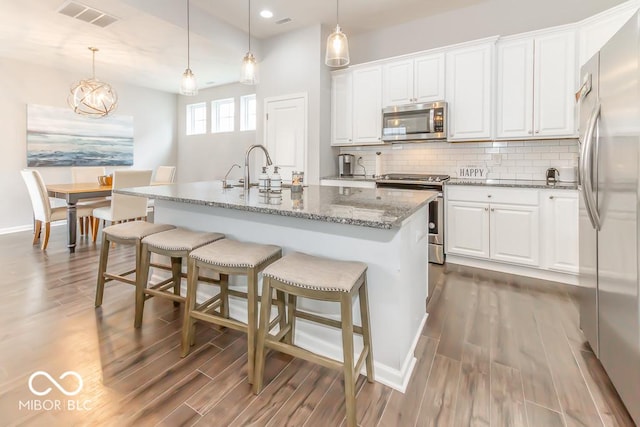 kitchen with pendant lighting, tasteful backsplash, white cabinetry, a kitchen island with sink, and stainless steel appliances