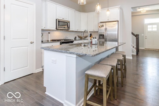 kitchen with appliances with stainless steel finishes, pendant lighting, white cabinetry, sink, and a center island with sink