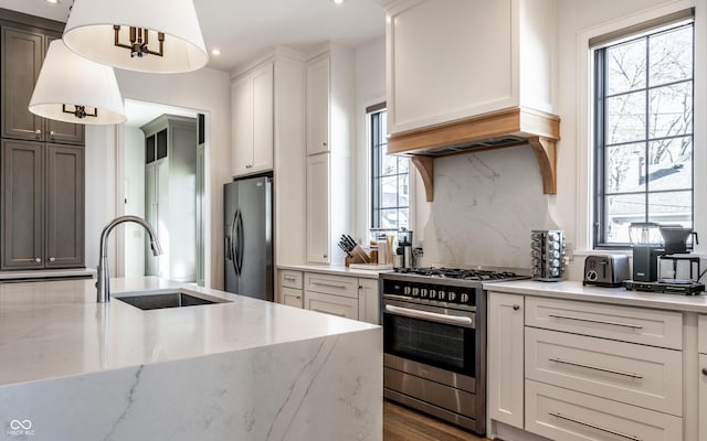 kitchen with sink, appliances with stainless steel finishes, white cabinetry, hanging light fixtures, and light stone countertops