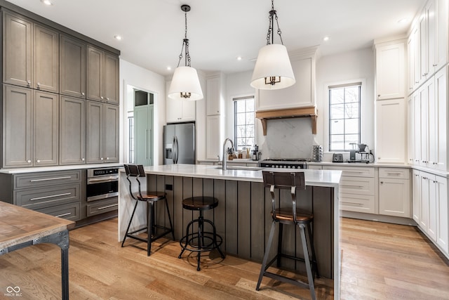 kitchen featuring gray cabinets, decorative light fixtures, an island with sink, a kitchen bar, and stainless steel appliances