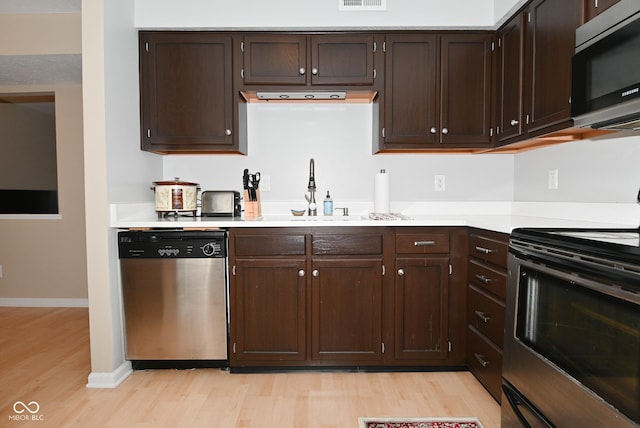 kitchen with stainless steel appliances, dark brown cabinets, sink, and light hardwood / wood-style floors