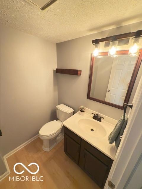 6639 N College Ave, Indianapolis, IN 46220 - half bathroom with vanity, toilet, wood finished floors, and a textured ceiling