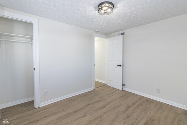 unfurnished bedroom featuring a textured ceiling, wood finished floors, visible vents, baseboards, and a closet