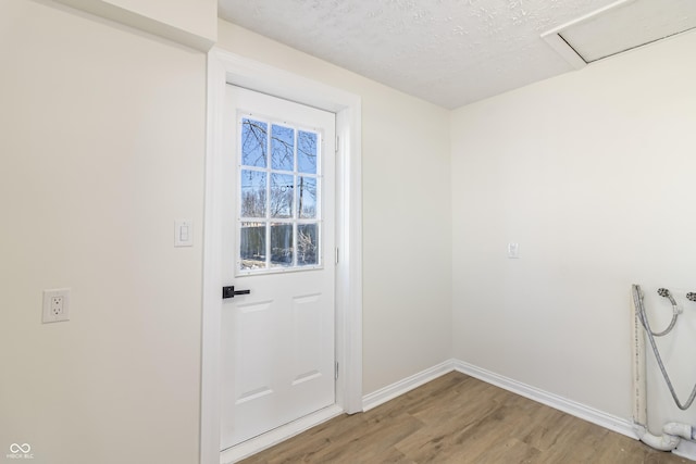 doorway with a textured ceiling, baseboards, and wood finished floors