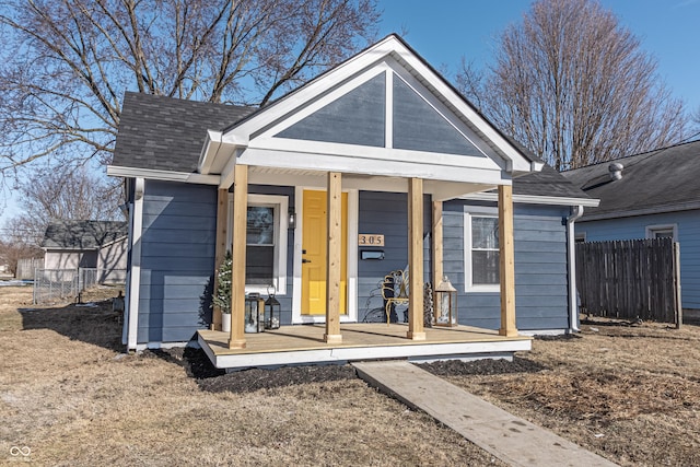 view of front of property with a shingled roof, covered porch, and fence