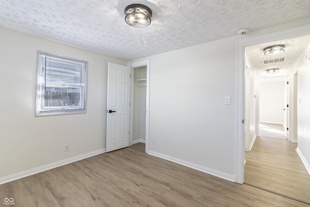 unfurnished bedroom with light wood-type flooring, visible vents, a textured ceiling, and baseboards