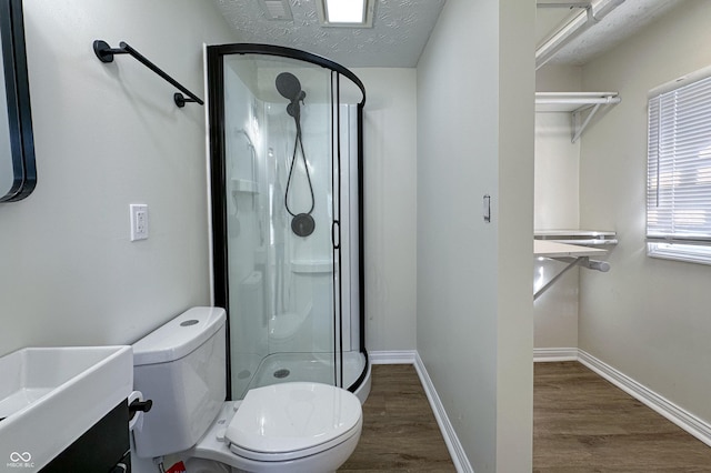 full bathroom with toilet, a shower stall, a textured ceiling, and wood finished floors