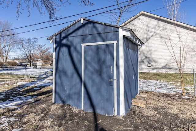 snow covered structure featuring fence, an outdoor structure, and a shed