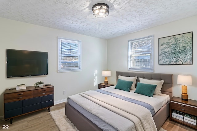 bedroom with a textured ceiling, multiple windows, baseboards, and light wood-style floors