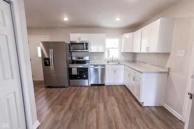 kitchen featuring stainless steel appliances, wood-type flooring, sink, and white cabinets