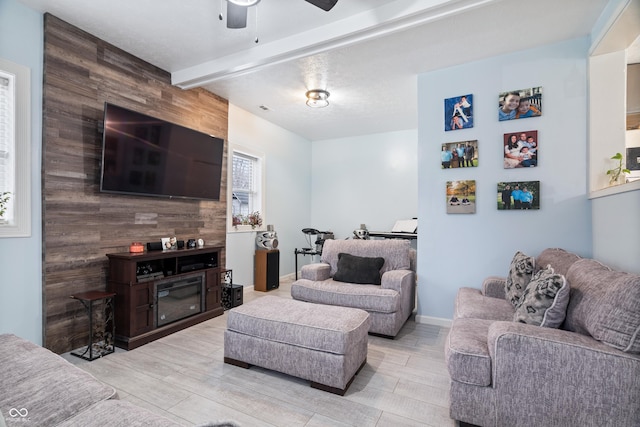 living room with beamed ceiling, ceiling fan, a large fireplace, and wooden walls