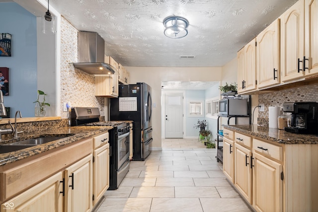 kitchen with wall chimney exhaust hood, sink, light brown cabinets, appliances with stainless steel finishes, and dark stone counters