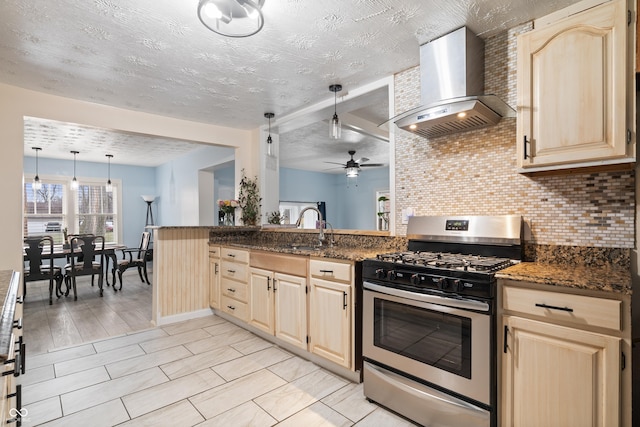 kitchen featuring stainless steel gas range, exhaust hood, decorative light fixtures, dark stone counters, and backsplash