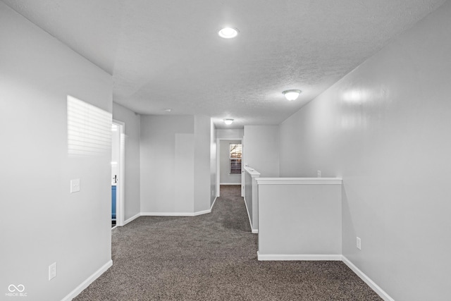 hall featuring dark carpet and a textured ceiling