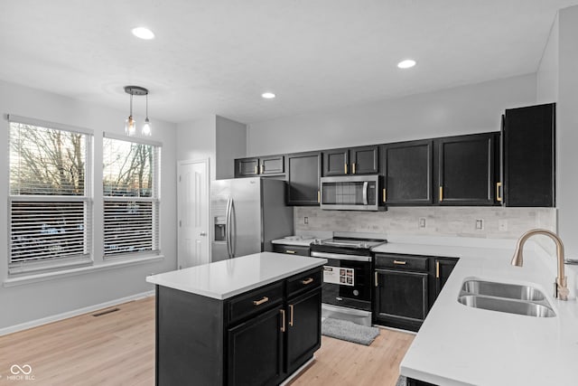 kitchen with decorative light fixtures, sink, decorative backsplash, stainless steel appliances, and light hardwood / wood-style flooring