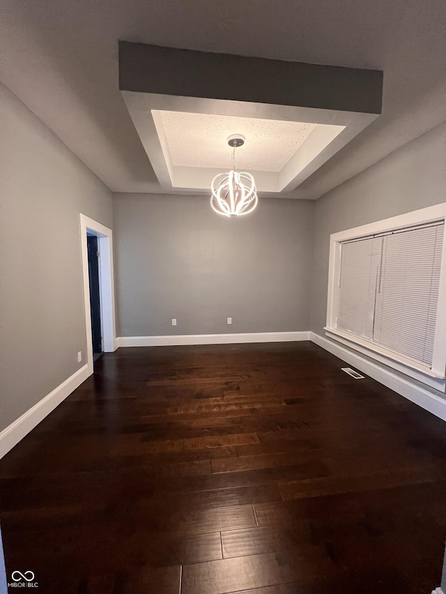 unfurnished dining area featuring dark wood-type flooring, a raised ceiling, and a notable chandelier