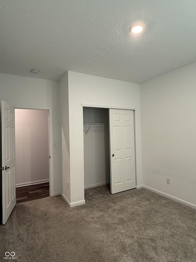 unfurnished bedroom with a textured ceiling, a closet, and dark colored carpet