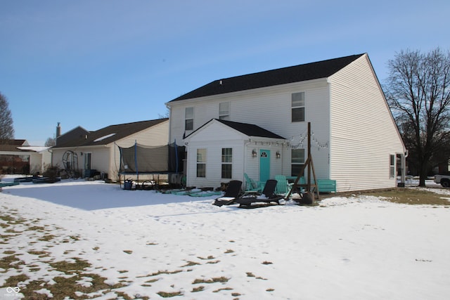 snow covered rear of property with a trampoline