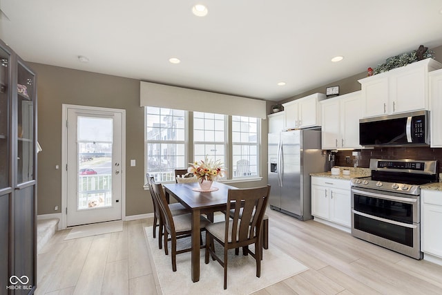 kitchen featuring light hardwood / wood-style flooring, white cabinetry, stainless steel appliances, light stone counters, and decorative backsplash