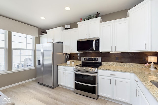 kitchen with stainless steel appliances, white cabinetry, light stone countertops, and tasteful backsplash