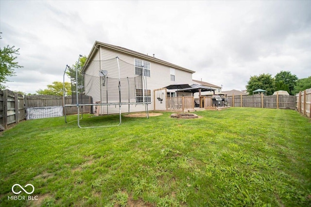 back of property with a gazebo, a trampoline, and a lawn