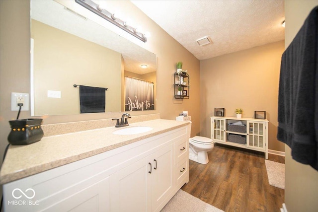 bathroom featuring wood-type flooring, vanity, a textured ceiling, and toilet