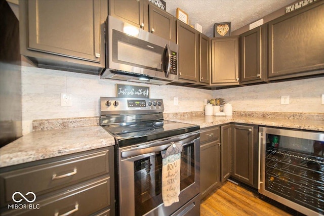 kitchen featuring wine cooler, light stone counters, light hardwood / wood-style flooring, appliances with stainless steel finishes, and backsplash