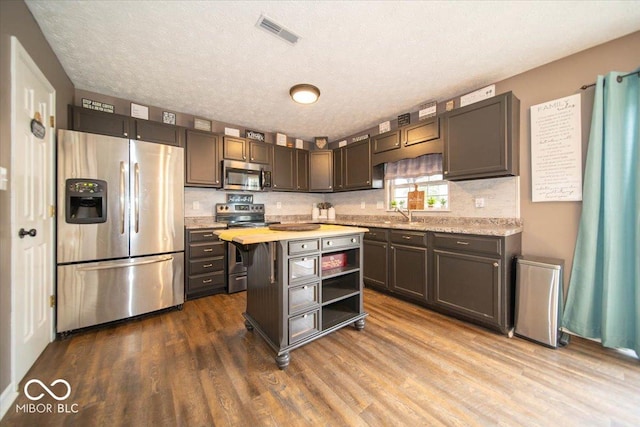 kitchen featuring butcher block counters, dark brown cabinets, appliances with stainless steel finishes, hardwood / wood-style flooring, and backsplash