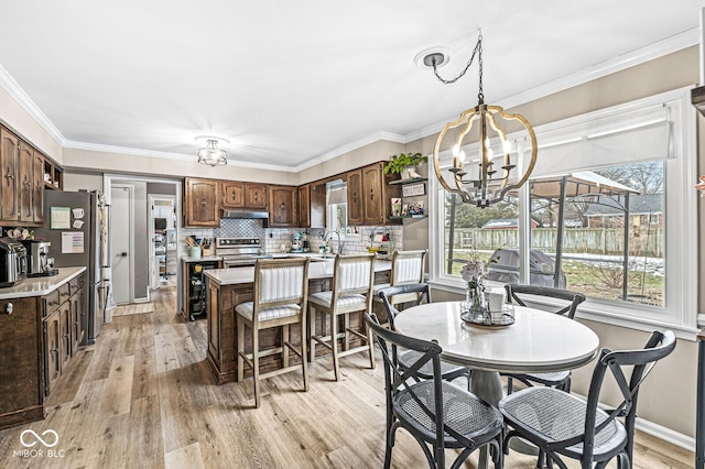 dining area featuring sink, ornamental molding, a chandelier, and light wood-type flooring