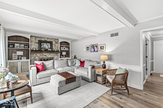 living room with crown molding, built in features, beam ceiling, a fireplace, and light hardwood / wood-style floors