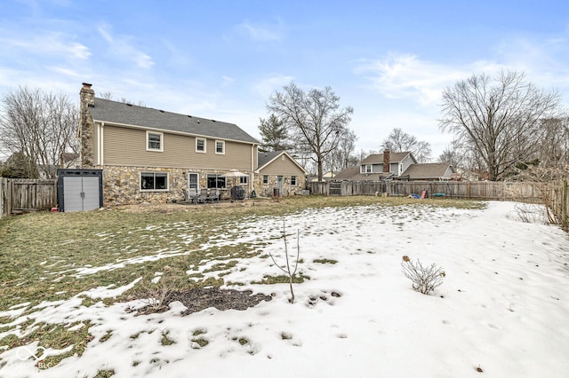 snow covered back of property featuring a storage unit and a yard