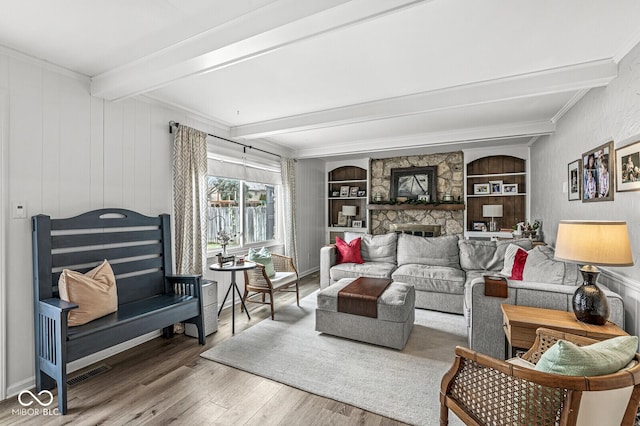 living room with wood-type flooring, a stone fireplace, built in features, and beam ceiling