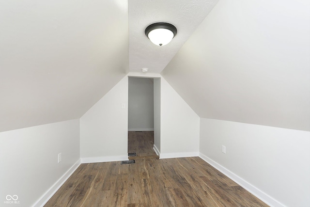 additional living space featuring a textured ceiling, lofted ceiling, visible vents, baseboards, and dark wood-style floors