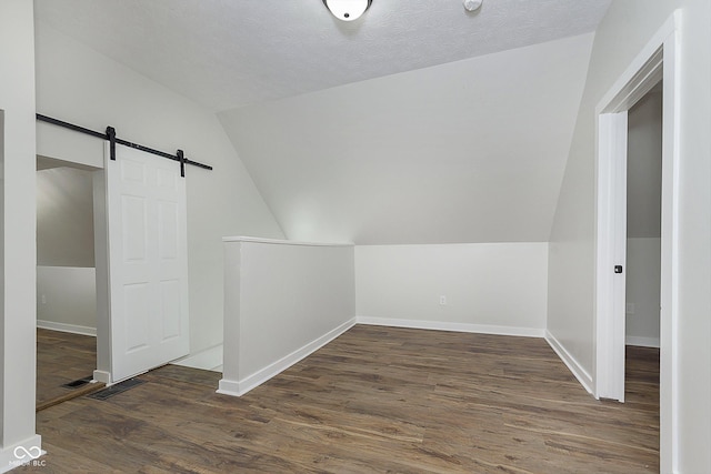 bonus room featuring dark wood finished floors, lofted ceiling, visible vents, a barn door, and baseboards