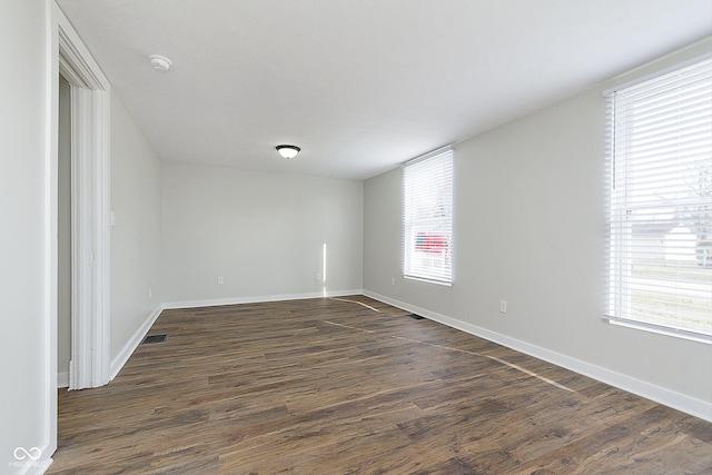 empty room with visible vents, baseboards, and dark wood finished floors