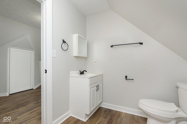 bathroom featuring toilet, wood finished floors, vanity, baseboards, and vaulted ceiling