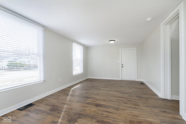 empty room featuring dark wood-type flooring, visible vents, and baseboards