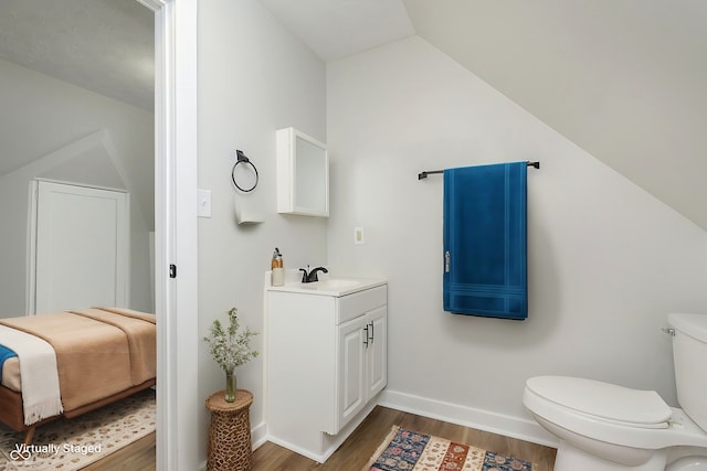 bathroom with lofted ceiling, toilet, wood finished floors, vanity, and baseboards