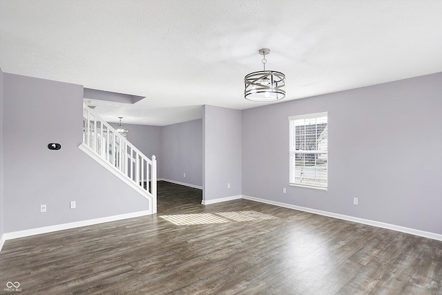 unfurnished living room with an inviting chandelier, dark hardwood / wood-style floors, and a textured ceiling