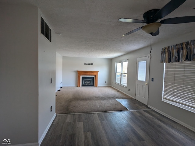 unfurnished living room with ceiling fan, dark hardwood / wood-style flooring, and a textured ceiling