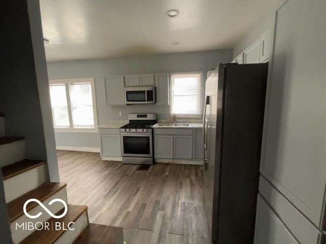 kitchen with sink, light wood-type flooring, white cabinets, and appliances with stainless steel finishes