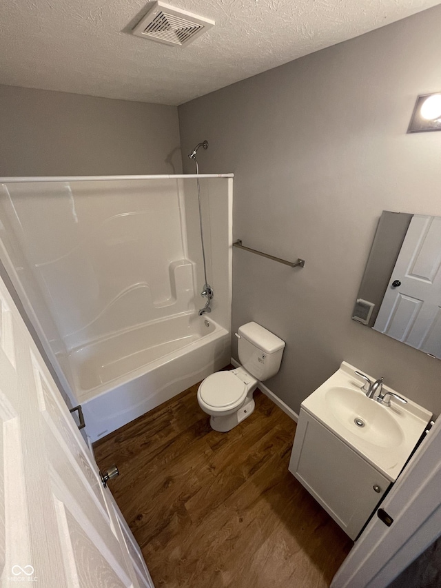 full bathroom with a textured ceiling, toilet, wood finished floors, visible vents, and shower / washtub combination