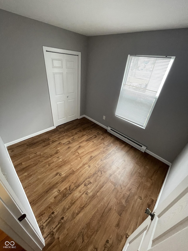 unfurnished bedroom with baseboards, a closet, a baseboard heating unit, and wood finished floors