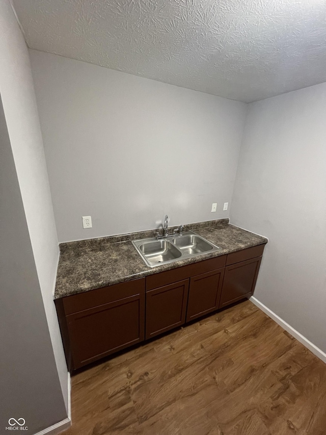 interior space featuring baseboards, a sink, a textured ceiling, and light wood finished floors