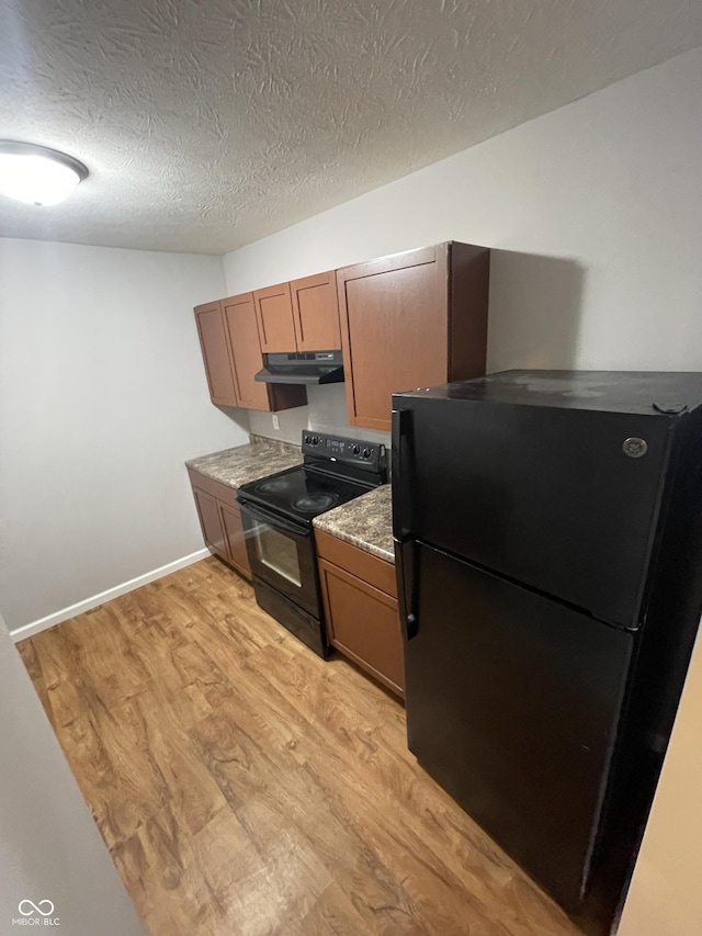 kitchen featuring black appliances, under cabinet range hood, light wood finished floors, and brown cabinetry